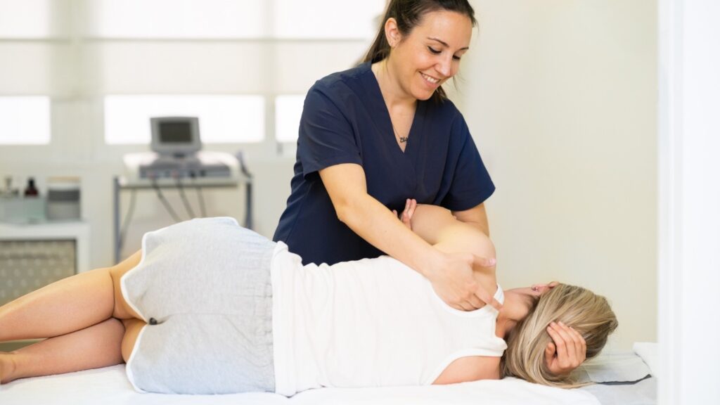 A chiropractor smiles while holding the arm of a patient during an adjustment.