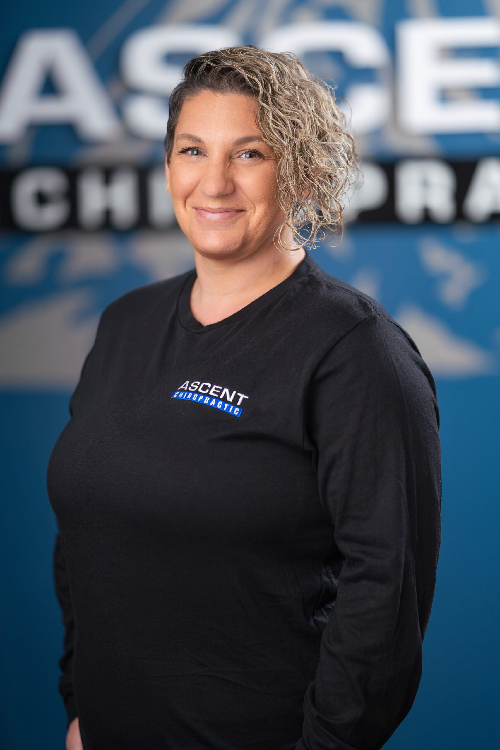 female with curly hair and ascent chiropactric logo shirt headshot