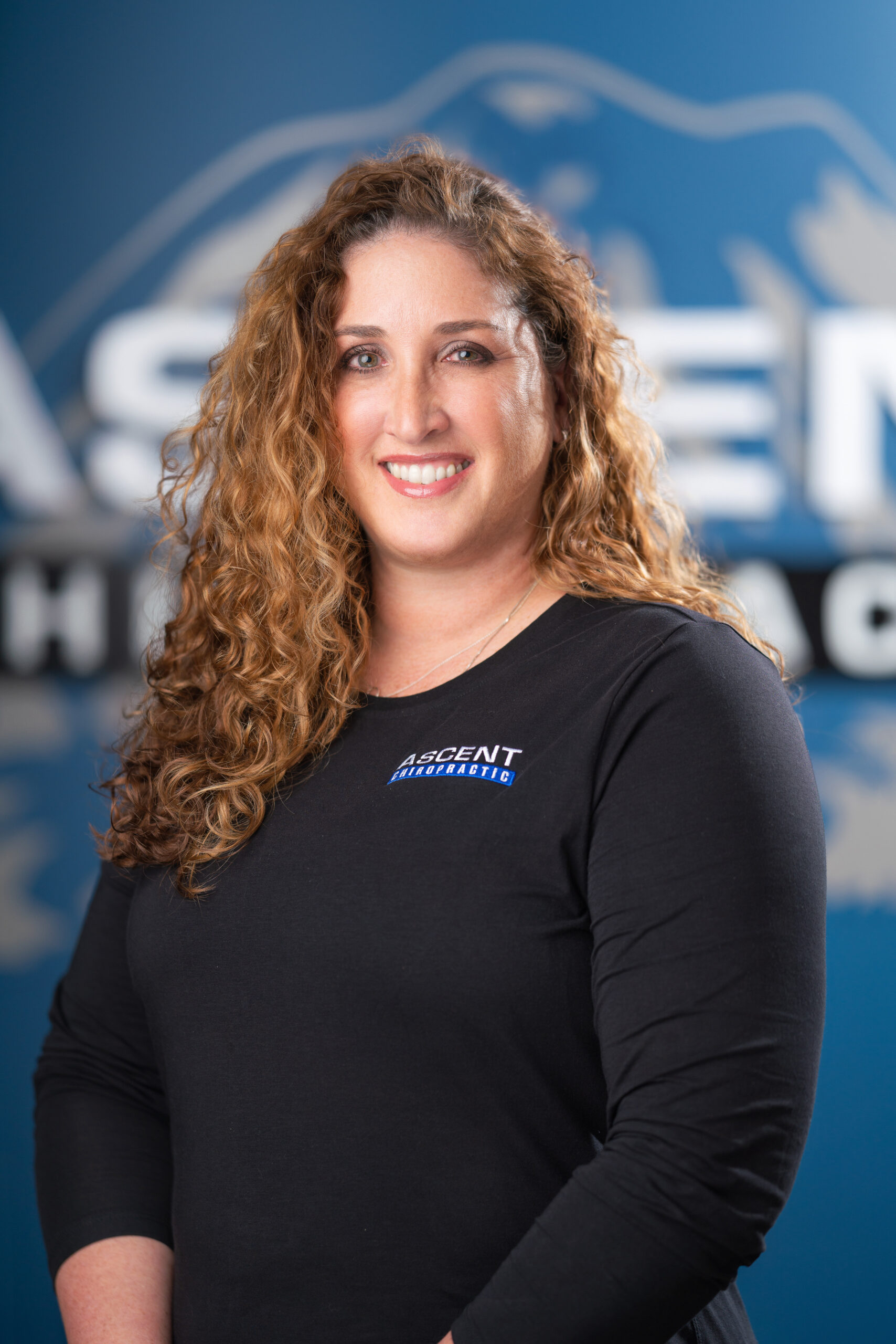 woman with light brown curly hair in an ascent chiropractic logo shirt headshot