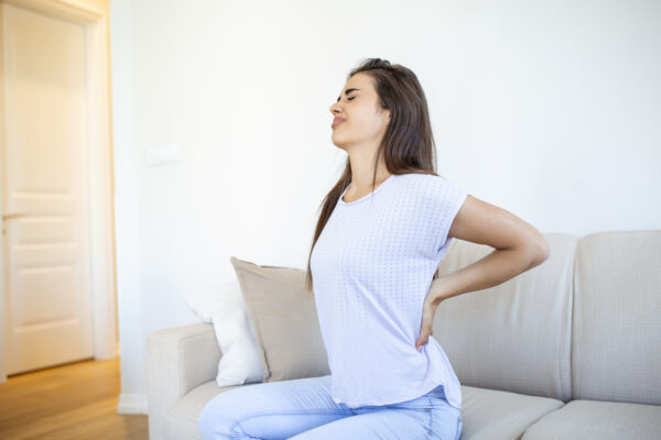 Woman in blue top and jeans stretching on a couch with her hands on her lower back
