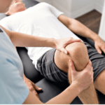 A chiropractor adjusts a man’s knee as he lies on a padded table.