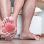 A man rubs his sore foot, there is a superimposed red effect on the painful area of the foot.