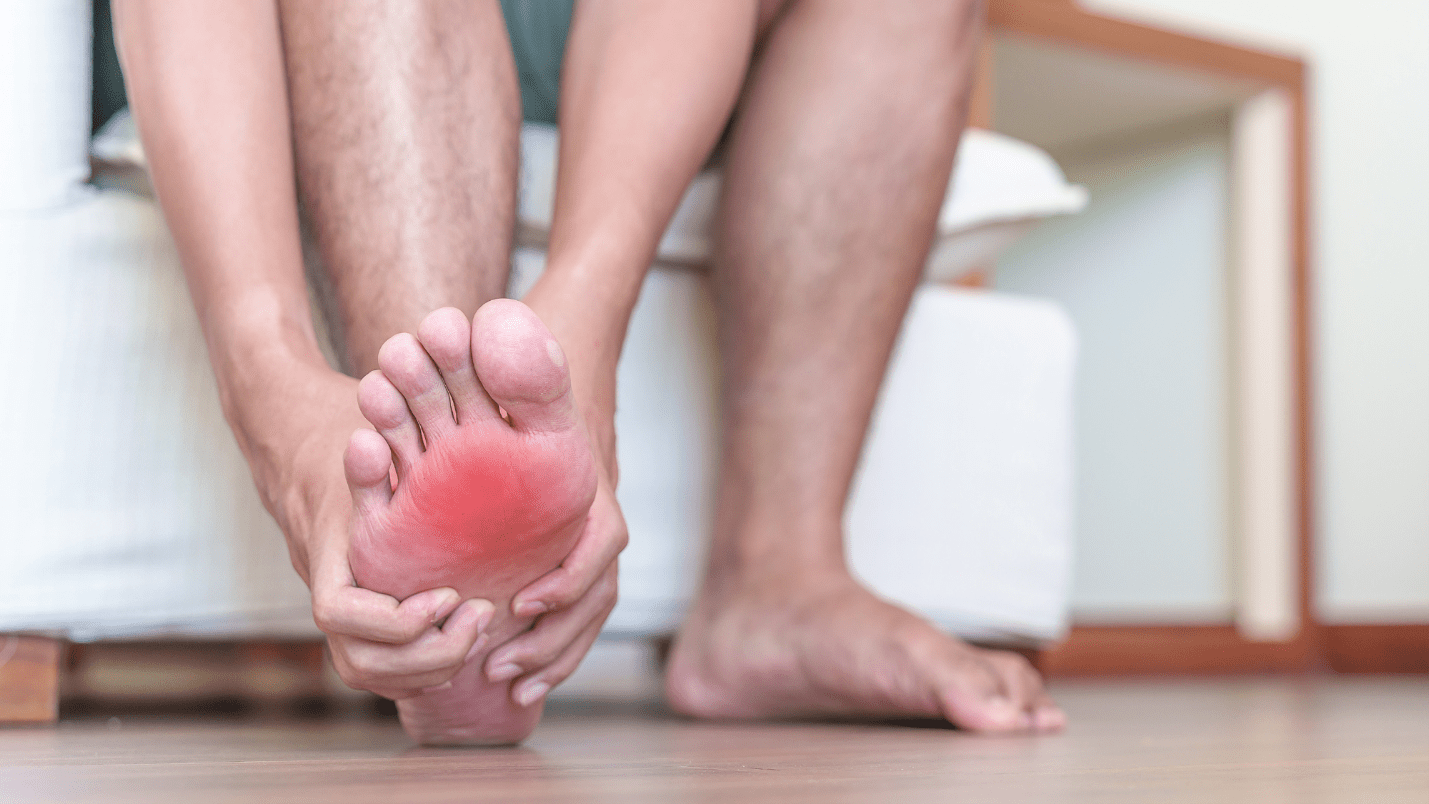 A man rubs his sore foot, there is a superimposed red effect on the painful area of the foot.