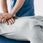 A man lays on a padded table while a chiropractor places hands on his lower back