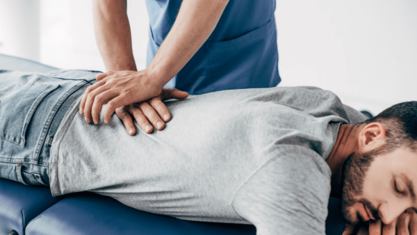 A man lays on a padded table while a chiropractor places hands on his lower back