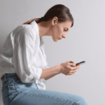 A person sits with poor posture, hunching over their phone.