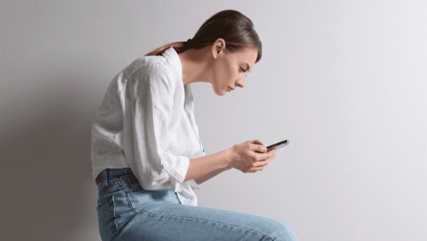 A person sits with poor posture, hunching over their phone.