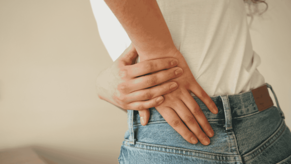 A person in jeans and a t-shirt touches their lower back, in pain.