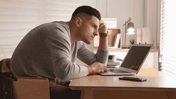 A worker hunches over a desk while working on a laptop.