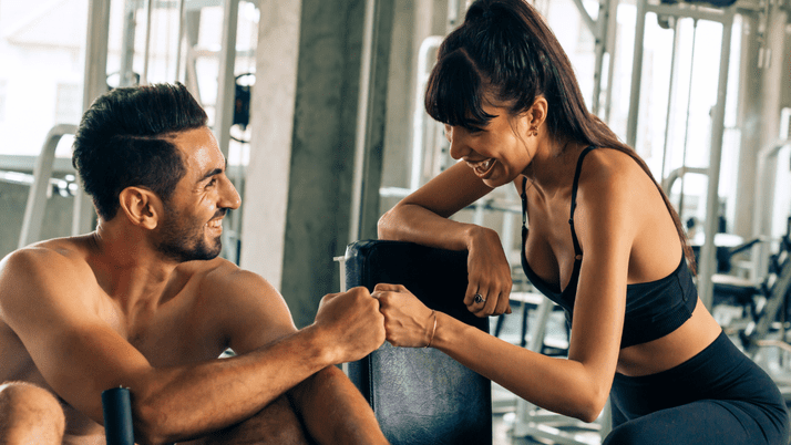 Two athletes at the gym smile and fist bump after a workout.