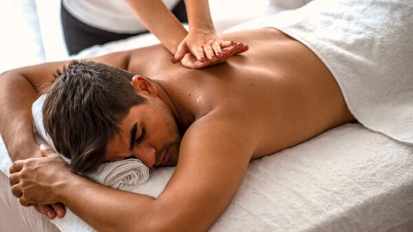 A man lays on a massage table, a masseuse kneads into his back.