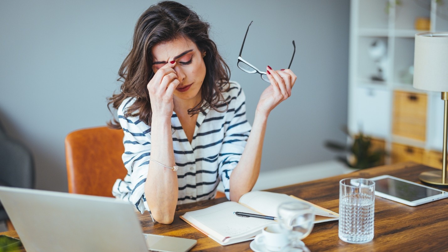 A woman in front of a laptop pinching the bridge of her nose, stressed out.