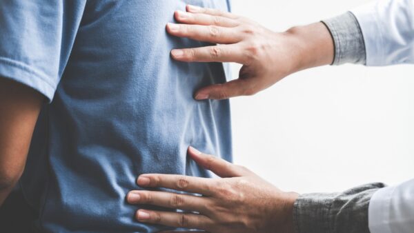 A chiropractor places hands on the back of a patient during a consultation.