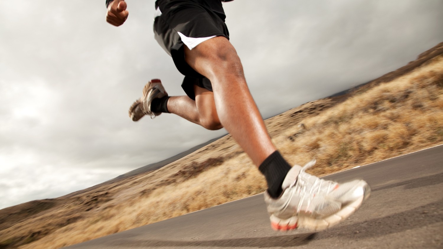 A man wearing athletic wear runs along an asphalt road.