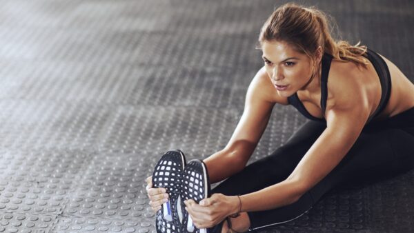 An athletic woman sits on the ground and stretches to hold her feet.