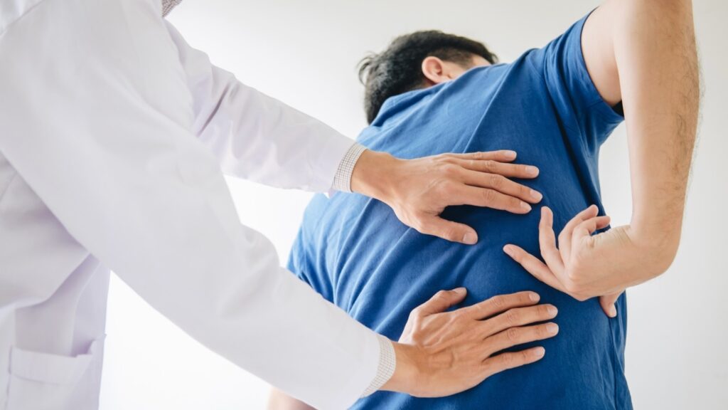 A man gestures where his back hurts while being examined by a chiropractor.